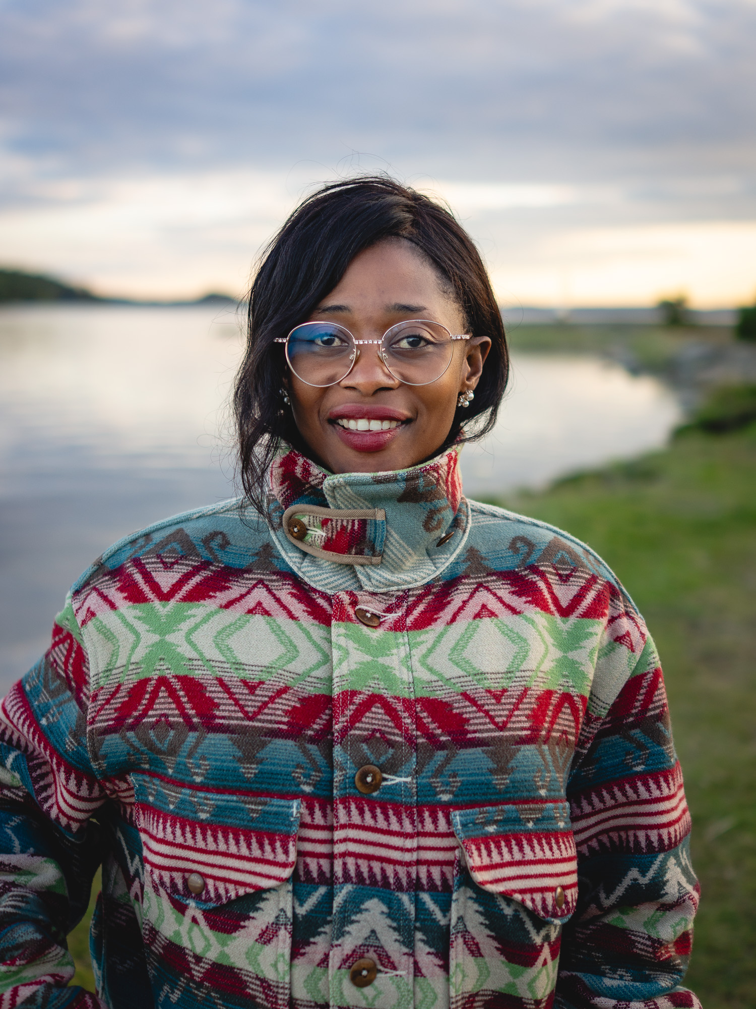 Jamirah smiling by the water at sunset in a patterned wool jacket