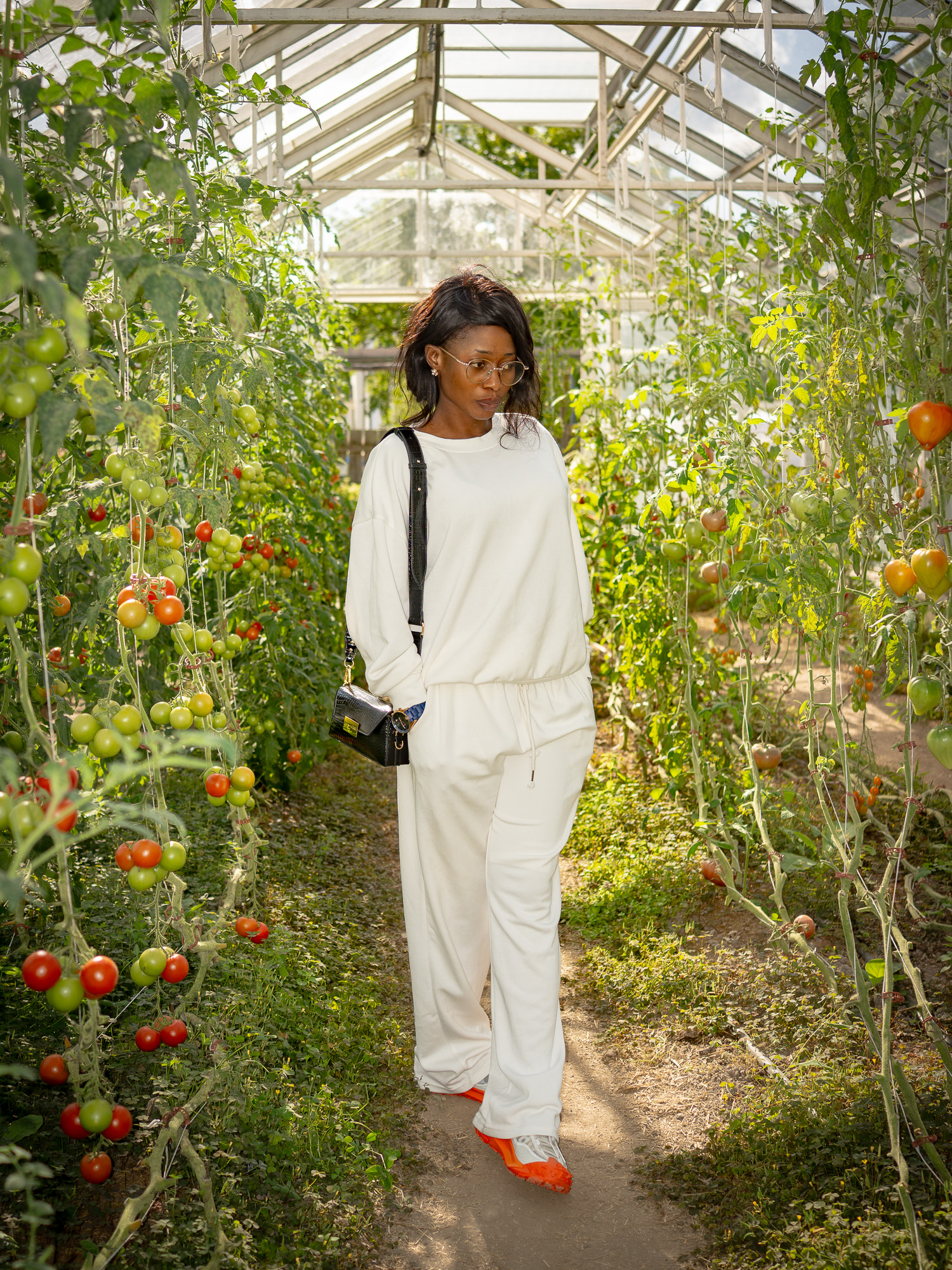 Jamirah in a cream outfit standing among tomato vines in a sunlit greenhouse
