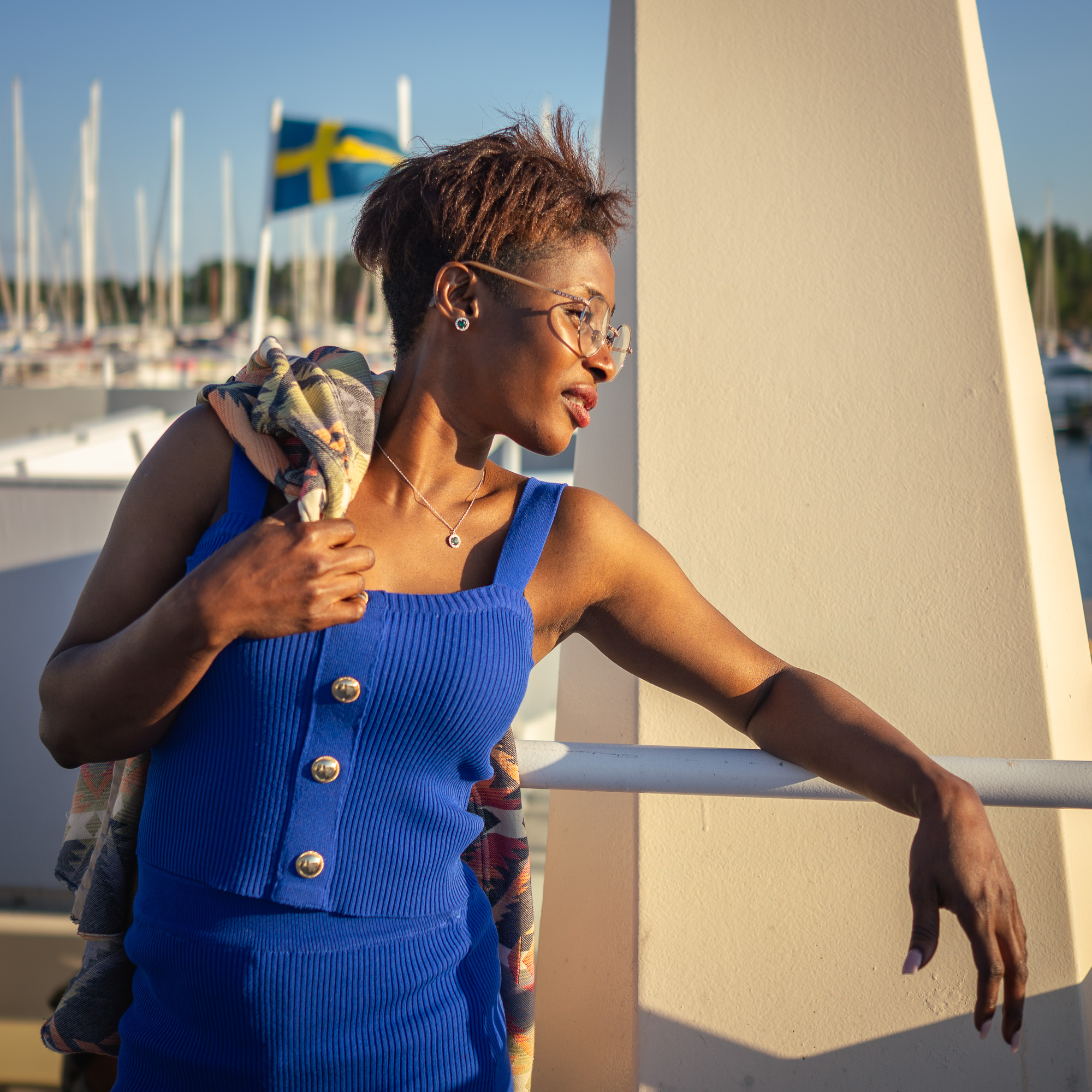 Jamirah in a blue knit set by a marina with the Swedish flag behind her