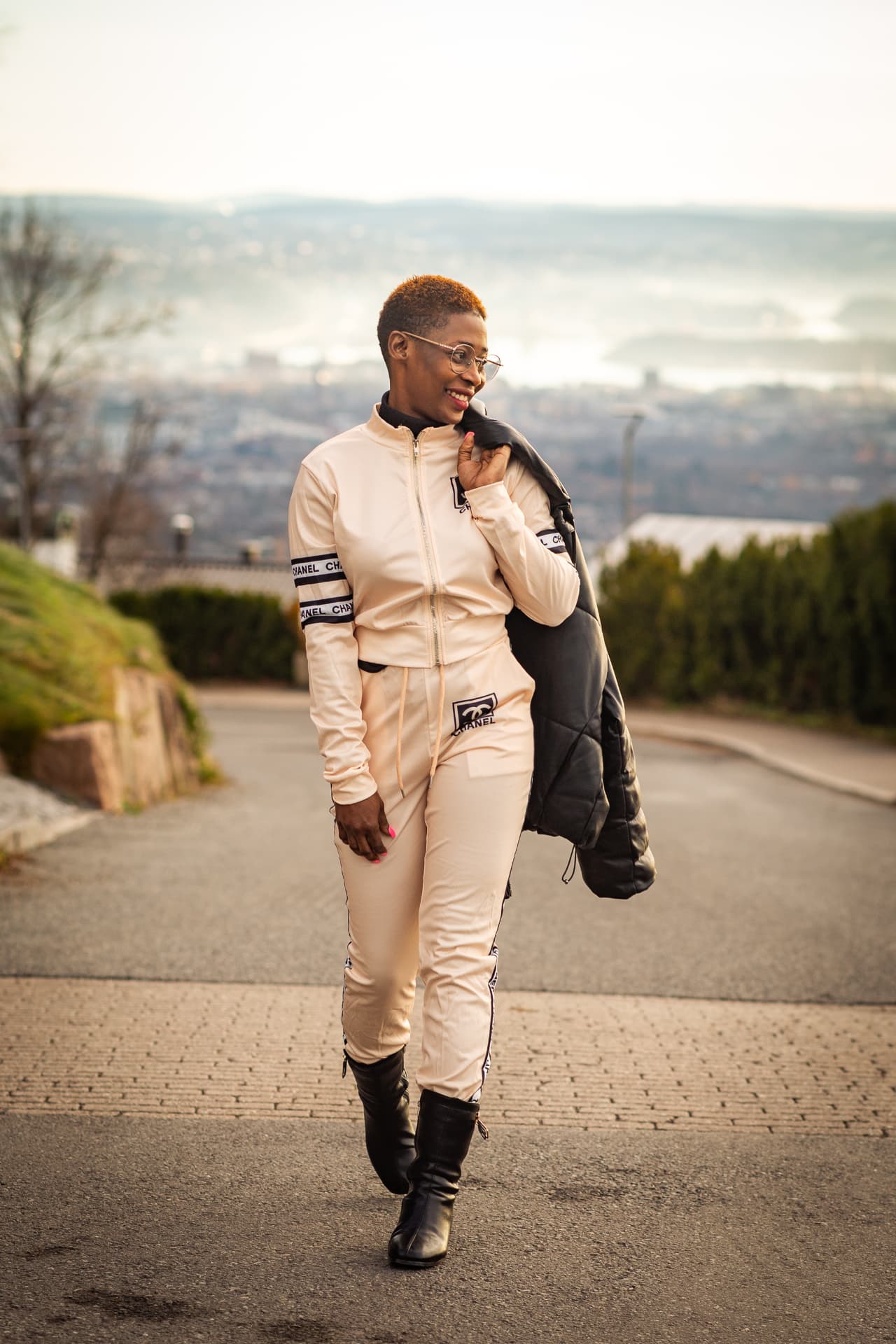 Jamirah walking on a hillside road overlooking Oslo, jacket over her shoulder